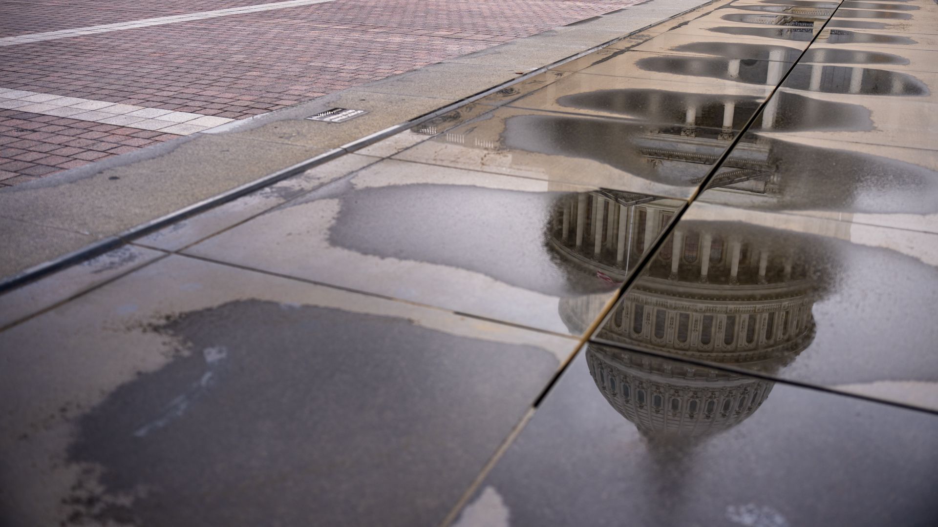 A reflection of the U.S. Capitol in a puddle on the ground.