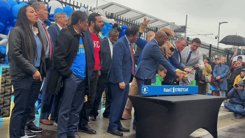 City leaders including KC Mayor Lucas push down a KC streetcar lever, flipping a ceremonial switch on the Main Street extension in front of a crowd with colorful fireworks shooting off in the background.