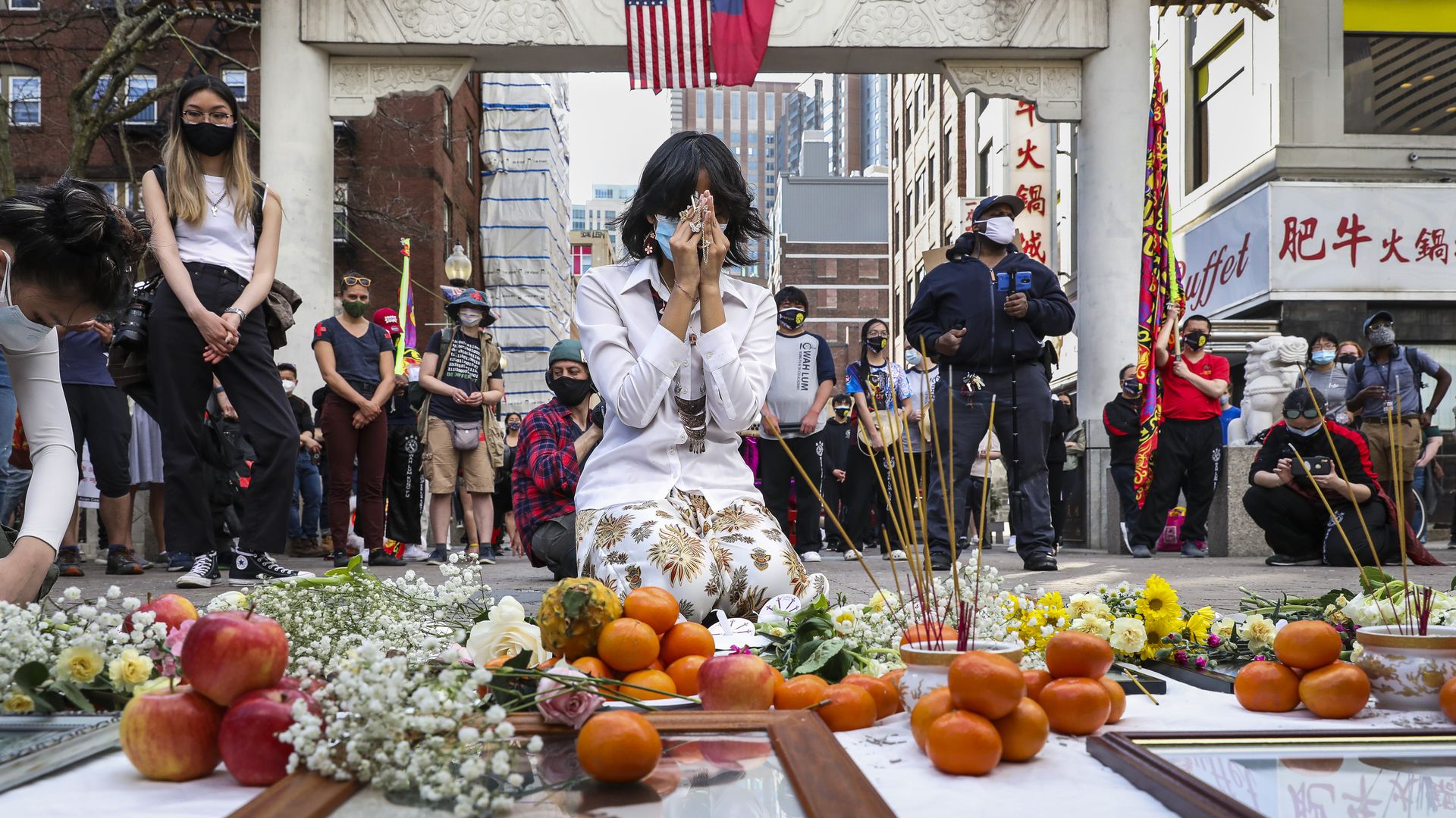 Photo of a person kneeling in front of the Boston Chinatown gates and honoring victims of anti-Asian violence with a moment of silence