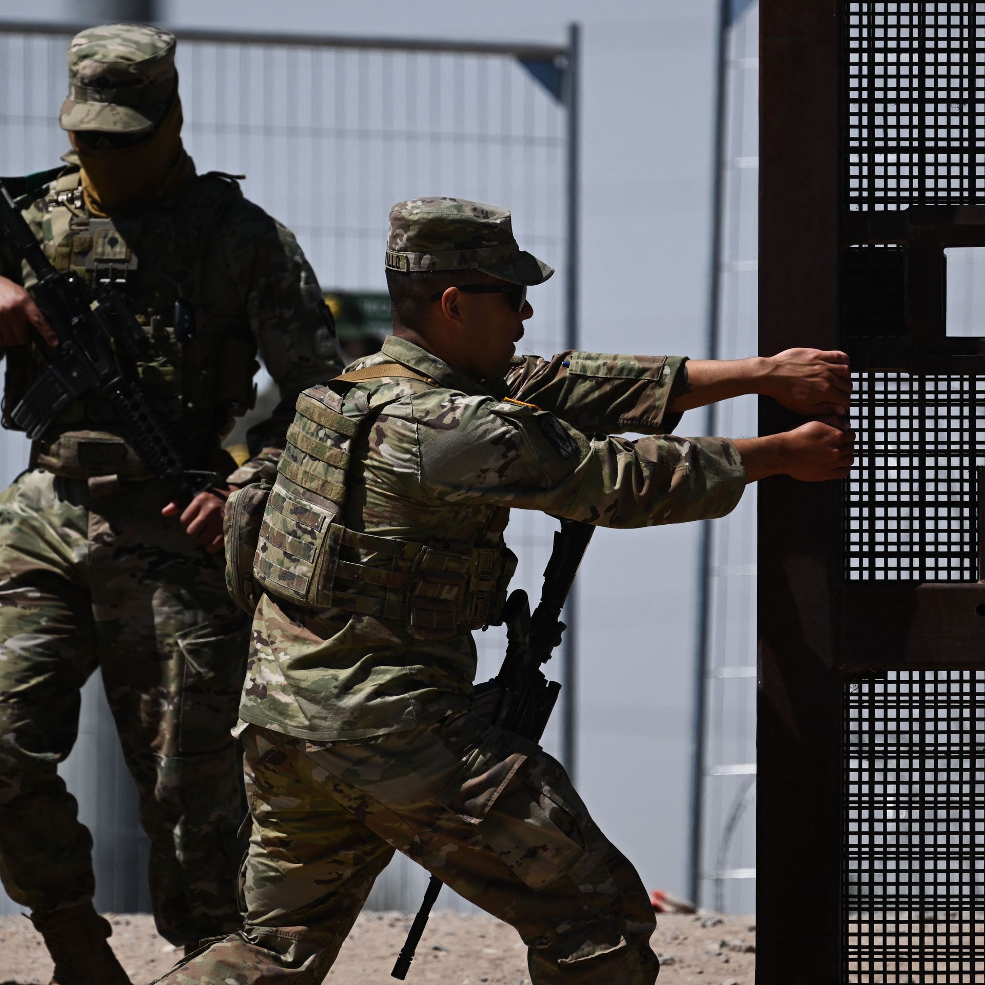 A member of the Texas Army National Guard closes a gate on the border wall as US Customs and Border Protection Border Patrol agents search migrants surrendering themselves for the processing of immigration and asylum claims on the US-Mexico border in El Paso, Texas 