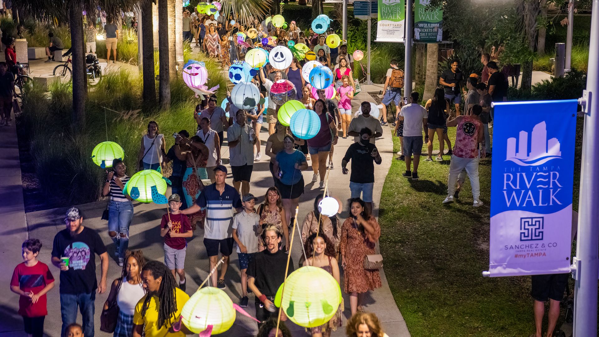 people walking with lanterns along the riverwalk