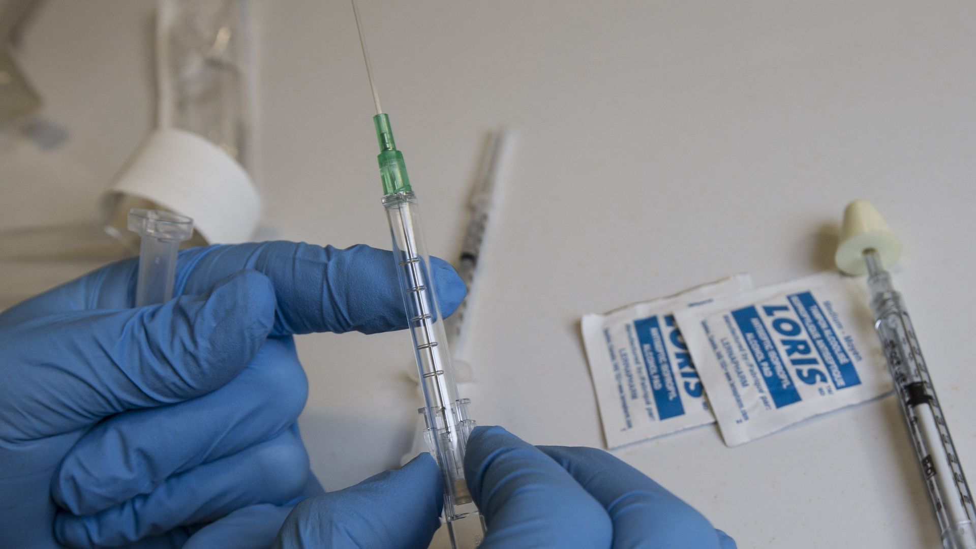 In this image, two gloved hands hold a needle.