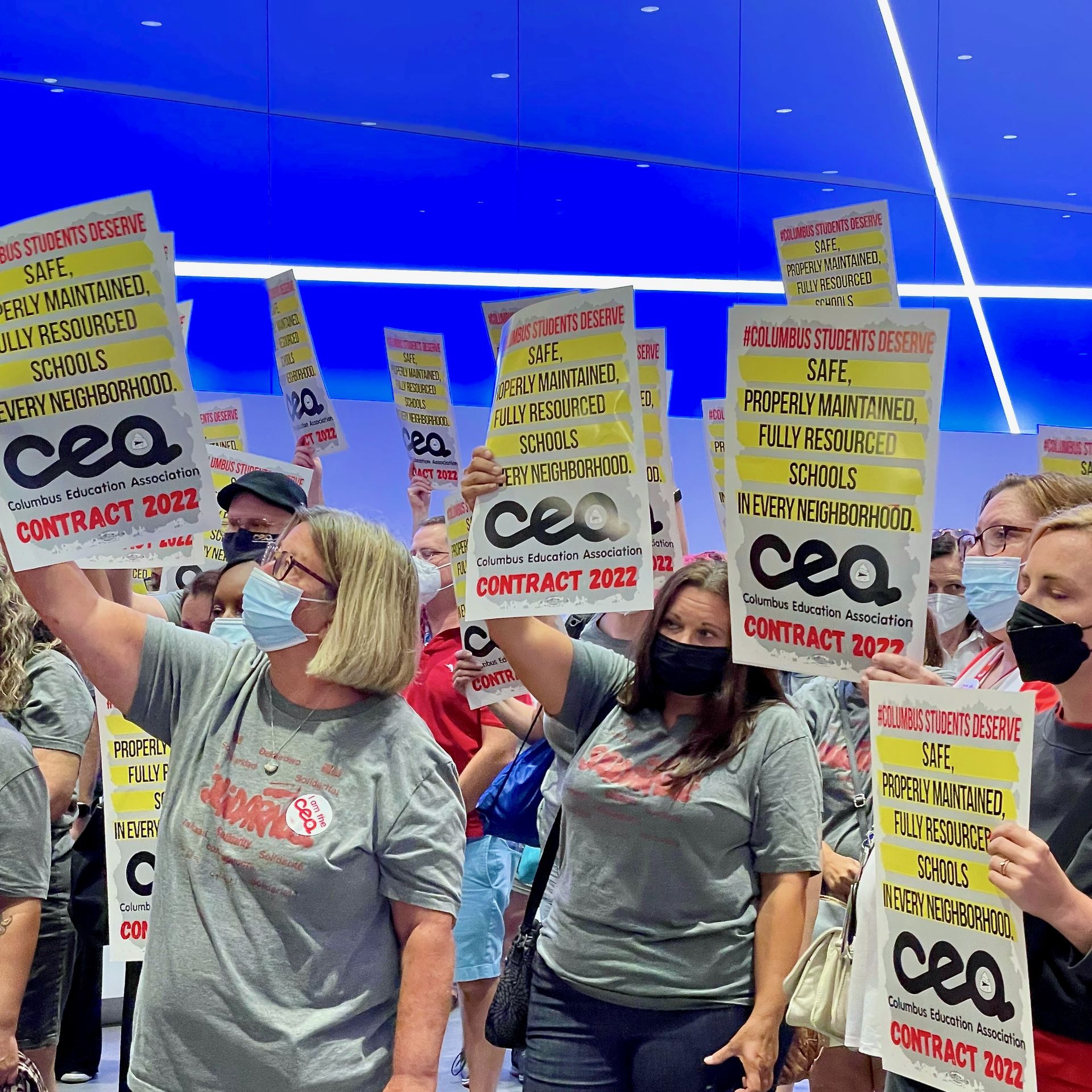Teachers hold signs  that say "Columbus students deserve safe, properly maintained, fully resourced schools in every neighborhood. Columbus Education Association contract 2022"