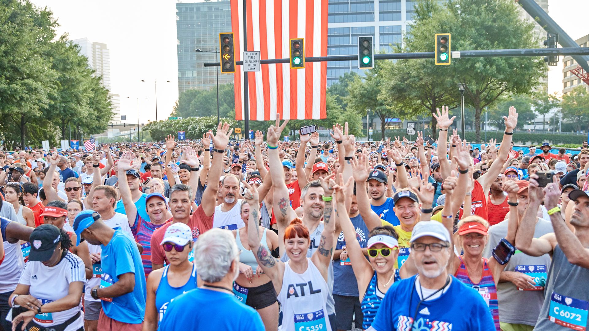 Runners at the Peachtree Road Race wave and greet the camera as a large U.S. flag hangs behind them
