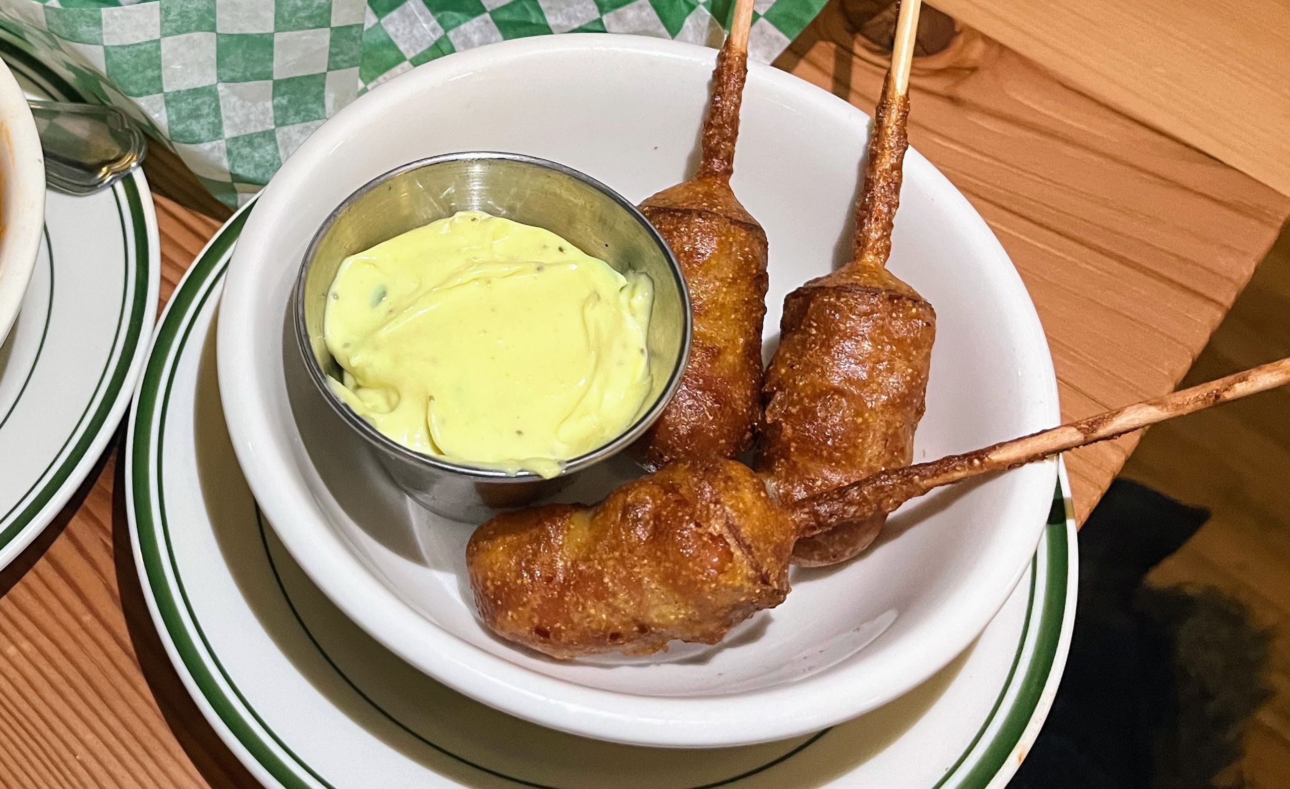 Corn dogs next to silver tin of yellow sauce.