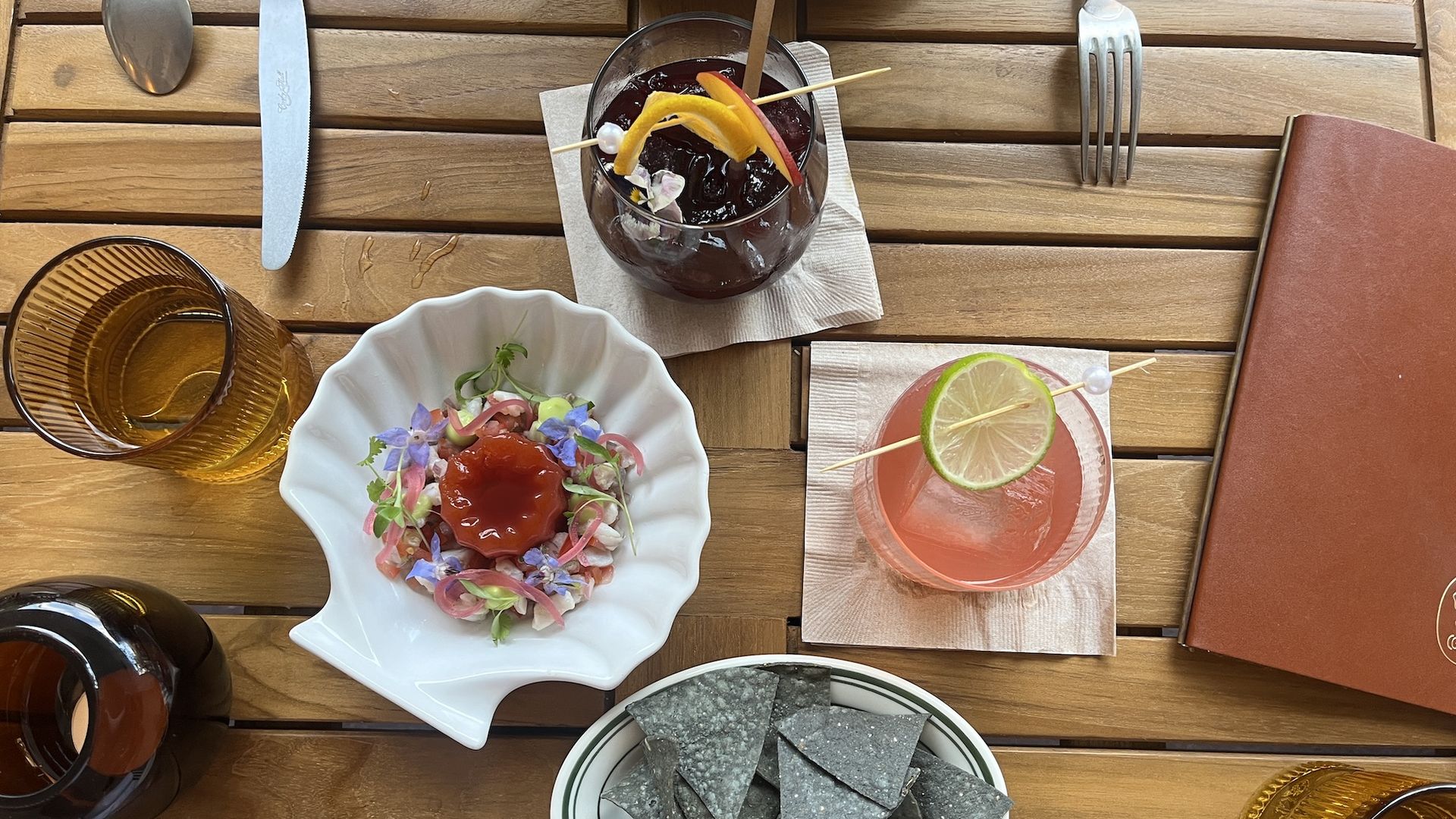 Two cocktails and a ceviche in a shell-shaped plate on a patio table.