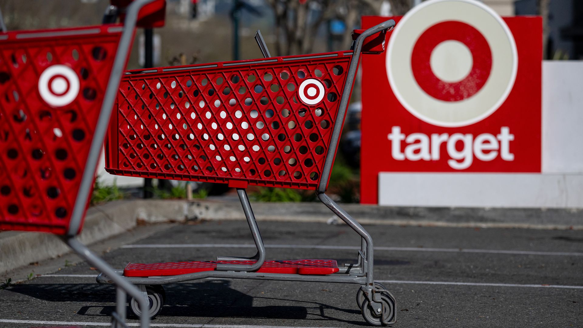 Red Target shopping carts with the Target logo, parked in an empty outdoor parking lot near a large red Target sign with the bullseye logo and white text.