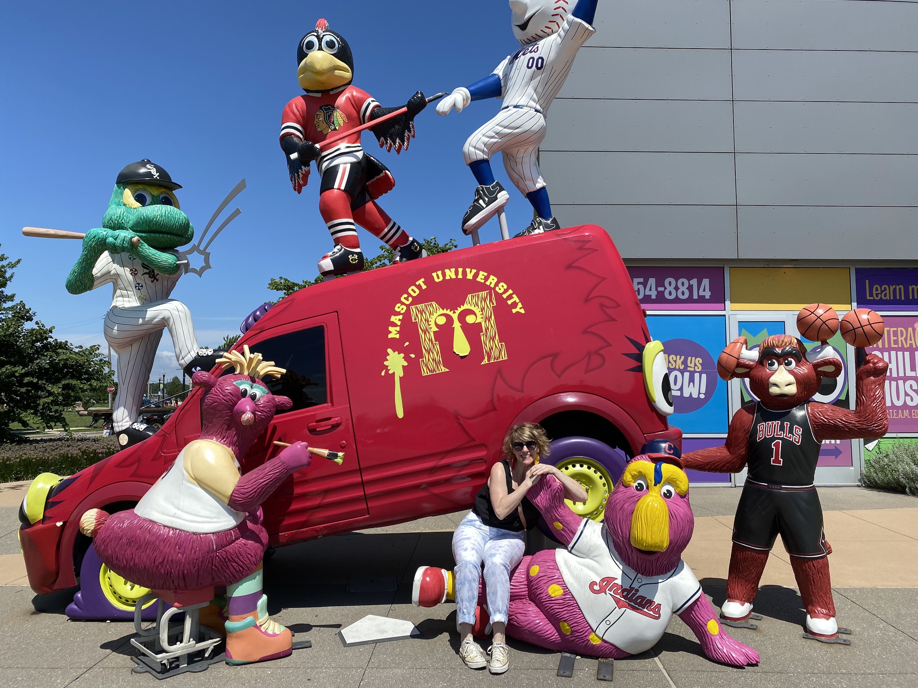 Large plastic figures of mascots climbing on a red truck, with woman sitting on one of the mascot's laps.