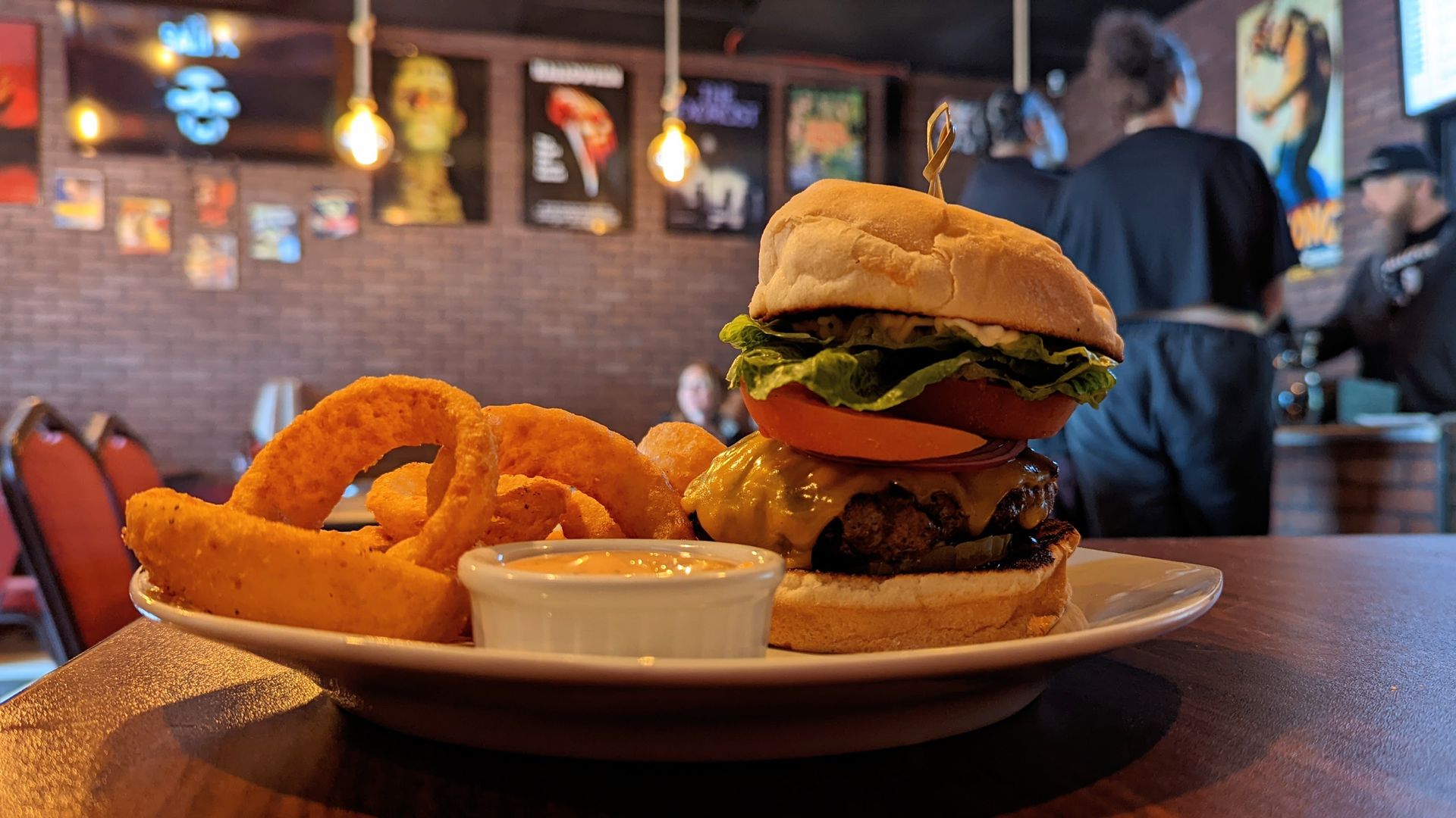 A towering cheeseburger with onion rings and condiments in a jar