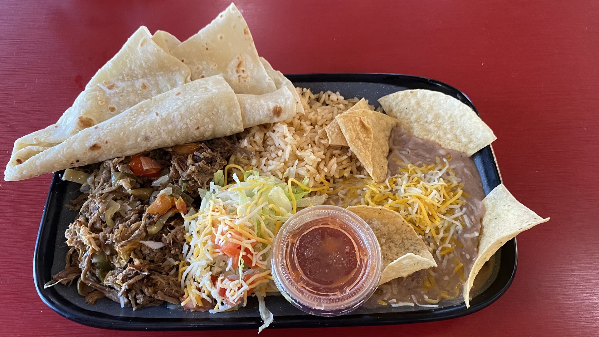 A rectangular plate with shredded beef, rice, refried beans and a tortilla.