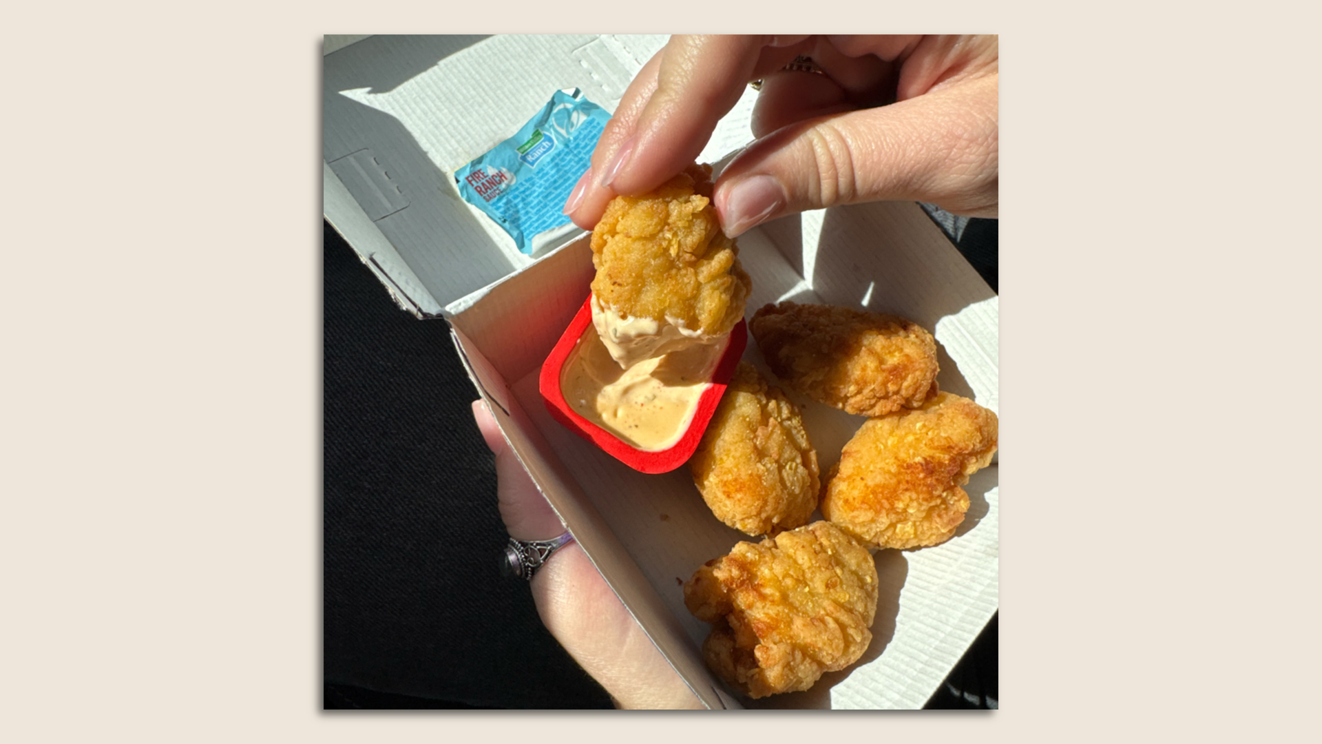Someone holds a chicken nugget after dipping it in a sauce