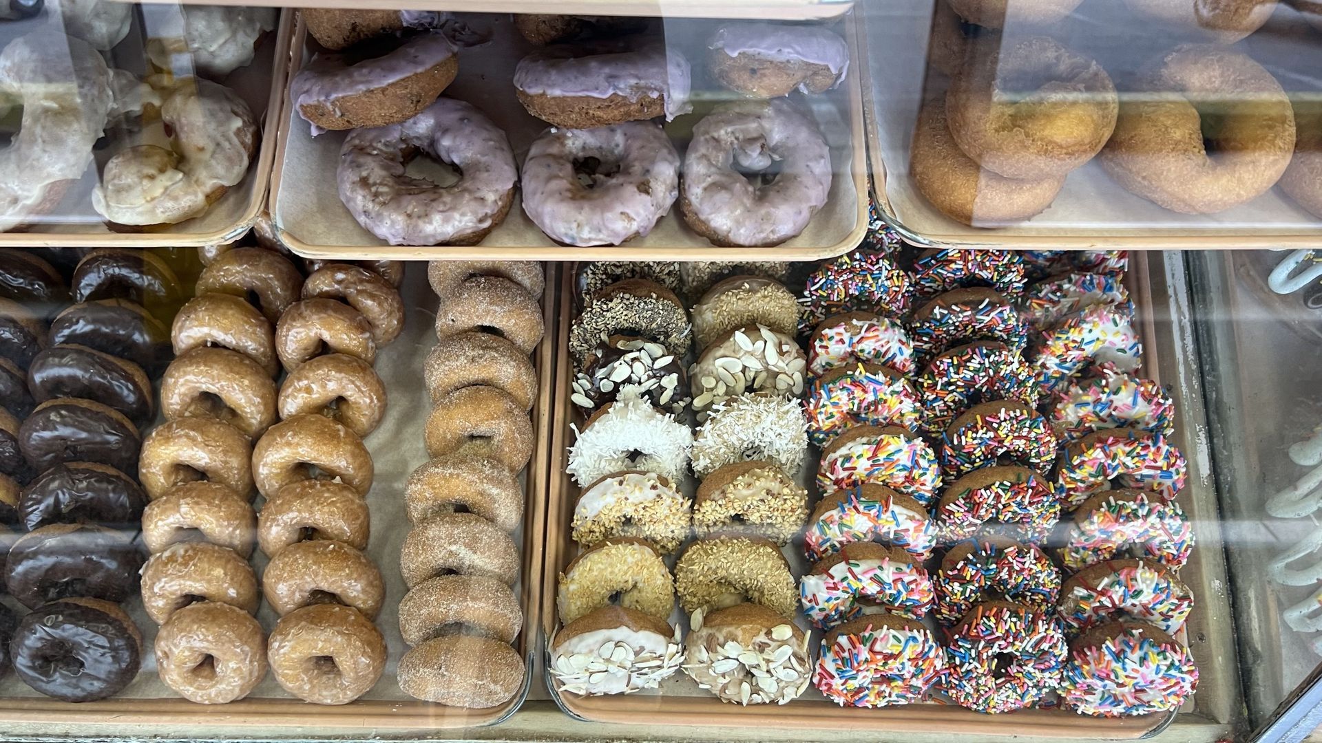 A bakery display case filled with trays of various types of donuts