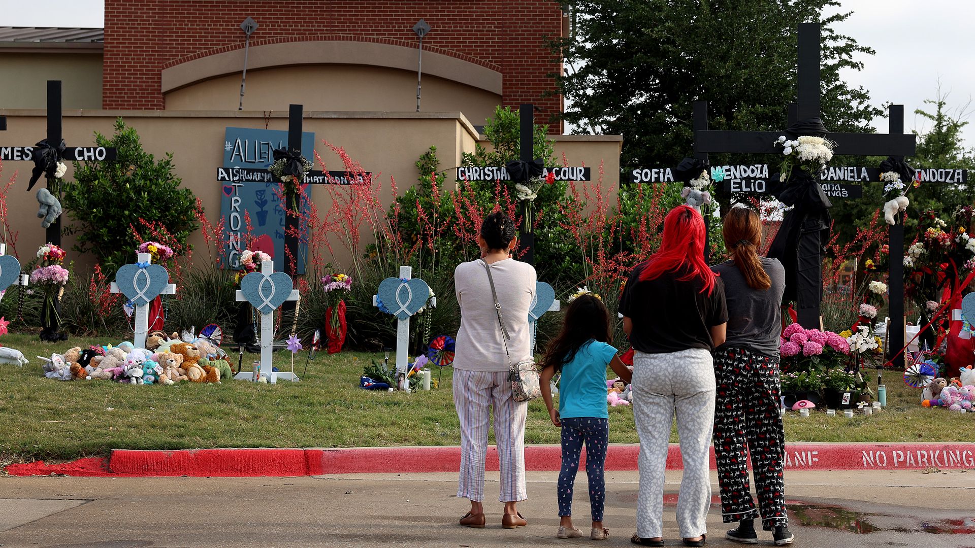 Four people stand in front of a memorial for the Allen shooting victims
