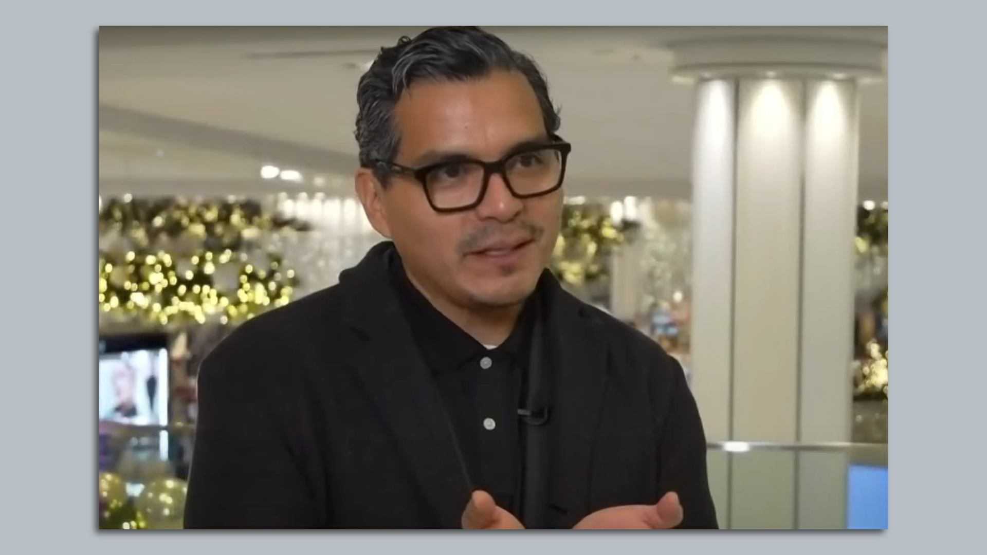 Manny Urquizo speaks to a camera with string lights behind him