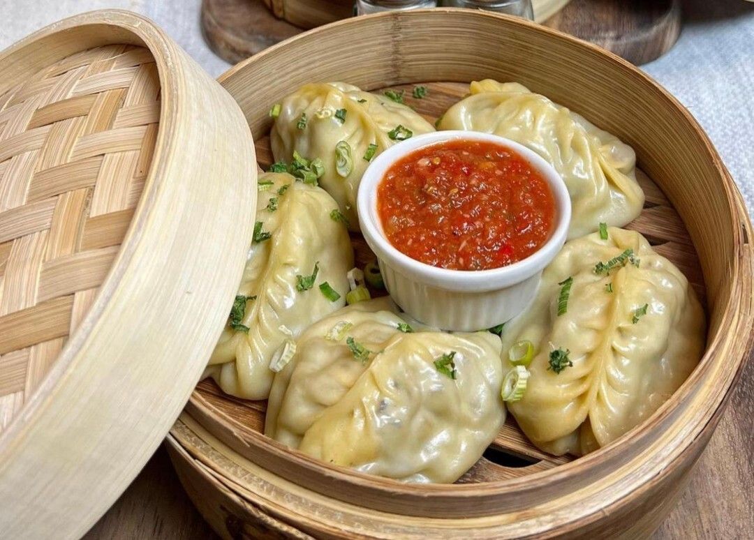 Five dumplings in a wooden basket, surrounding a red dip.