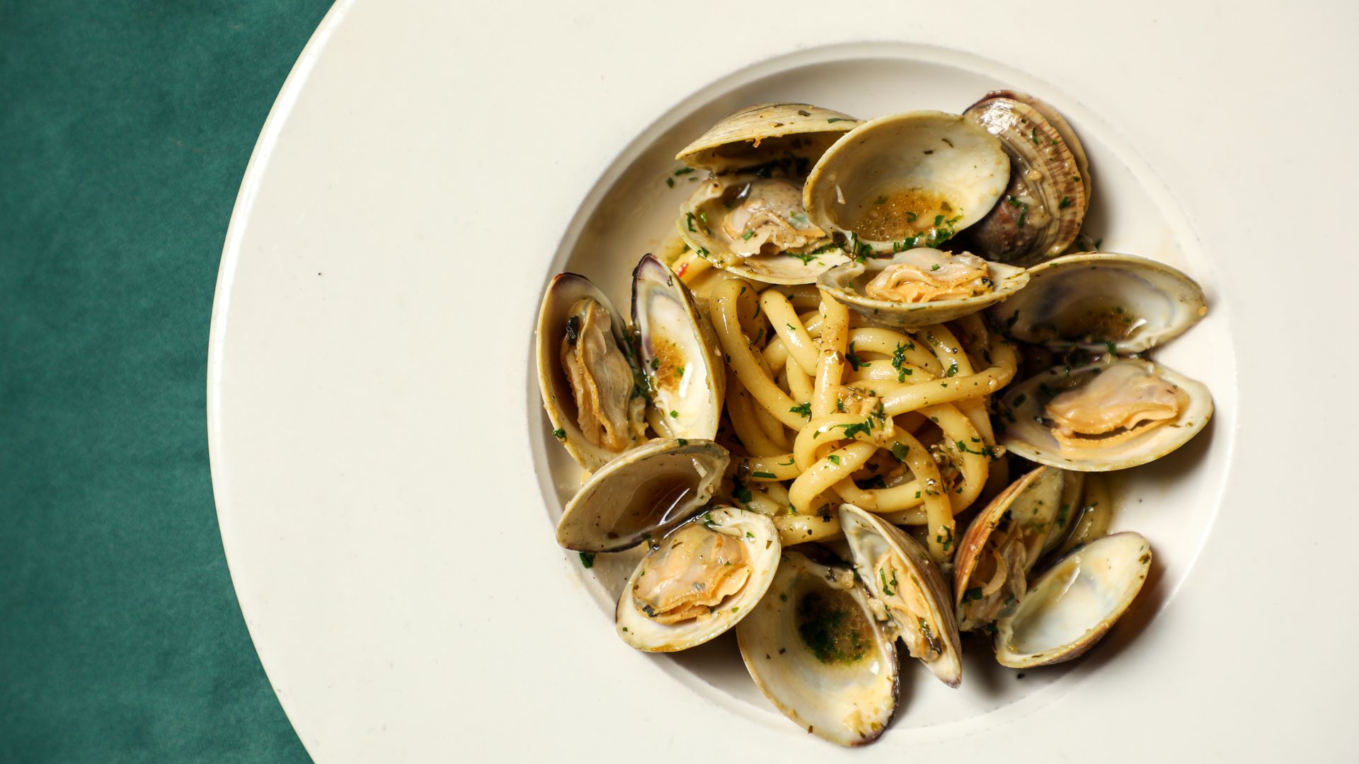 Photo shows cooked clams with linguini in a white bowl