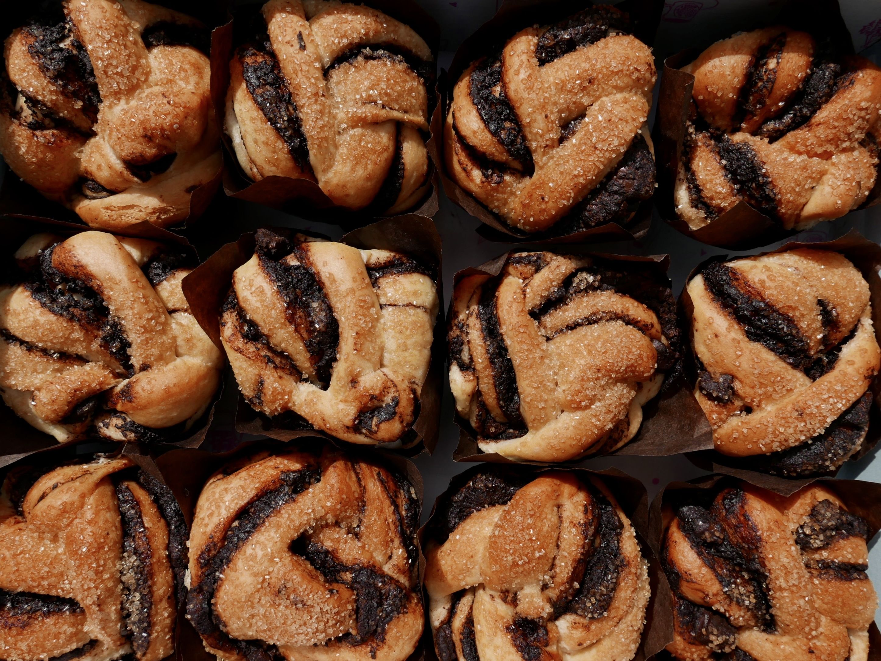 Close-up of sugar-crusted cinnamon buns with dark chocolate swirls, baked in brown paper liners and arranged in neat rows.
