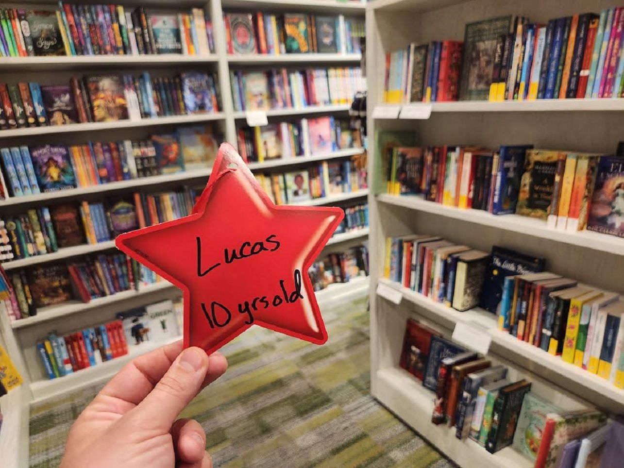 Holding up a star ornament reading "Lucas, 10 yrs old" in front of bookshelves. 