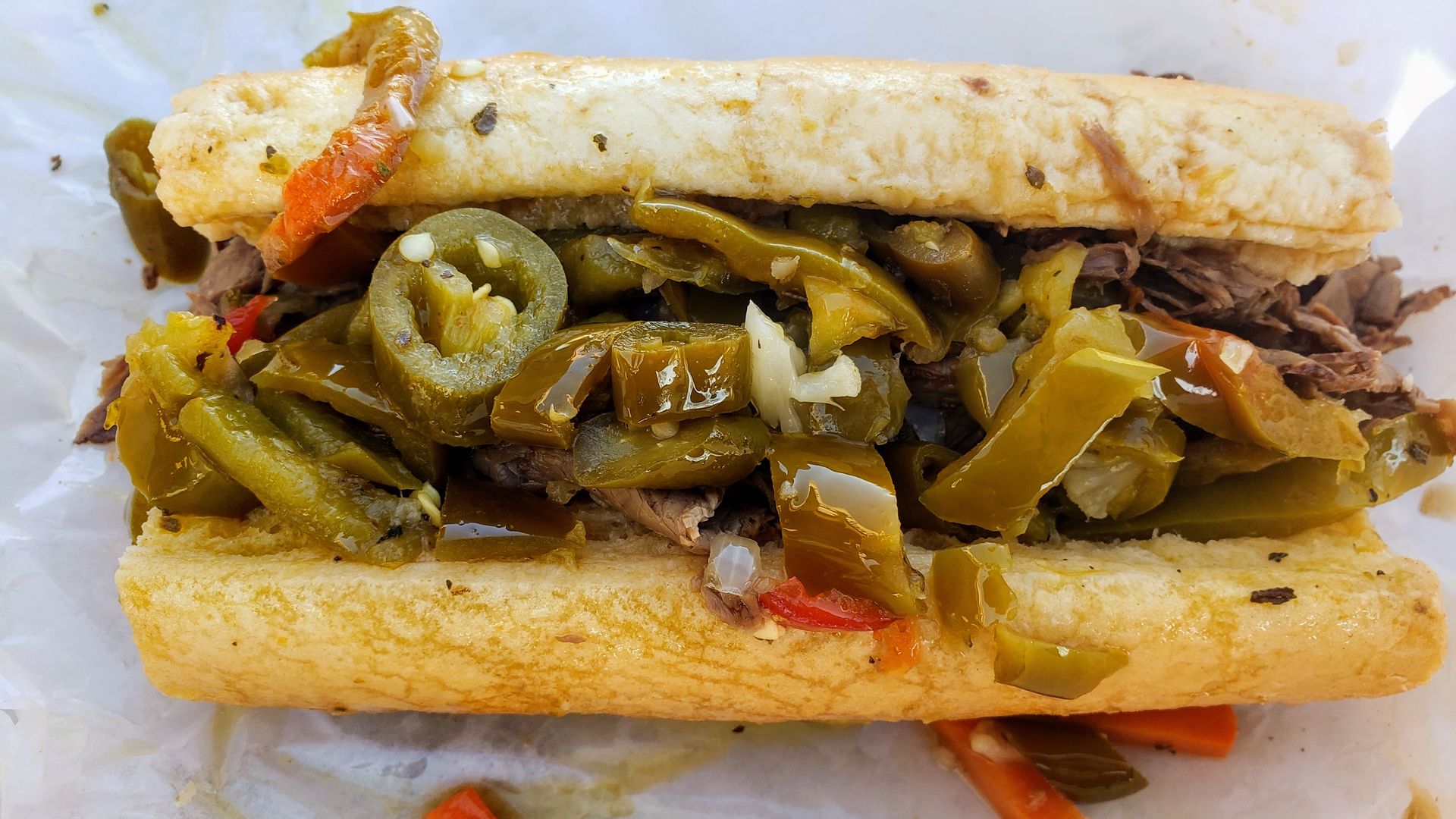 Photo of an Italian beef sandwich, with green and orange peppers. 