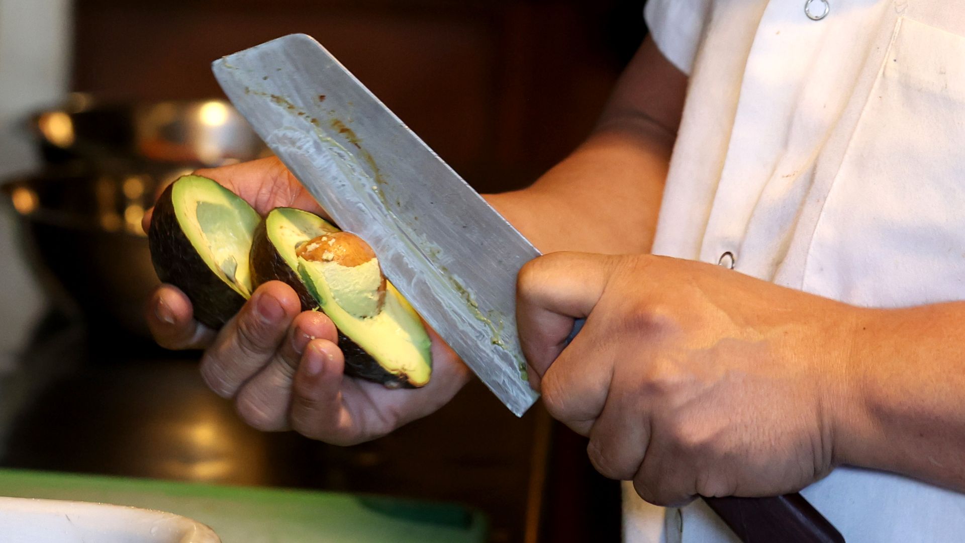 Photo of a person slicing an avocado with a knife in a kitchen