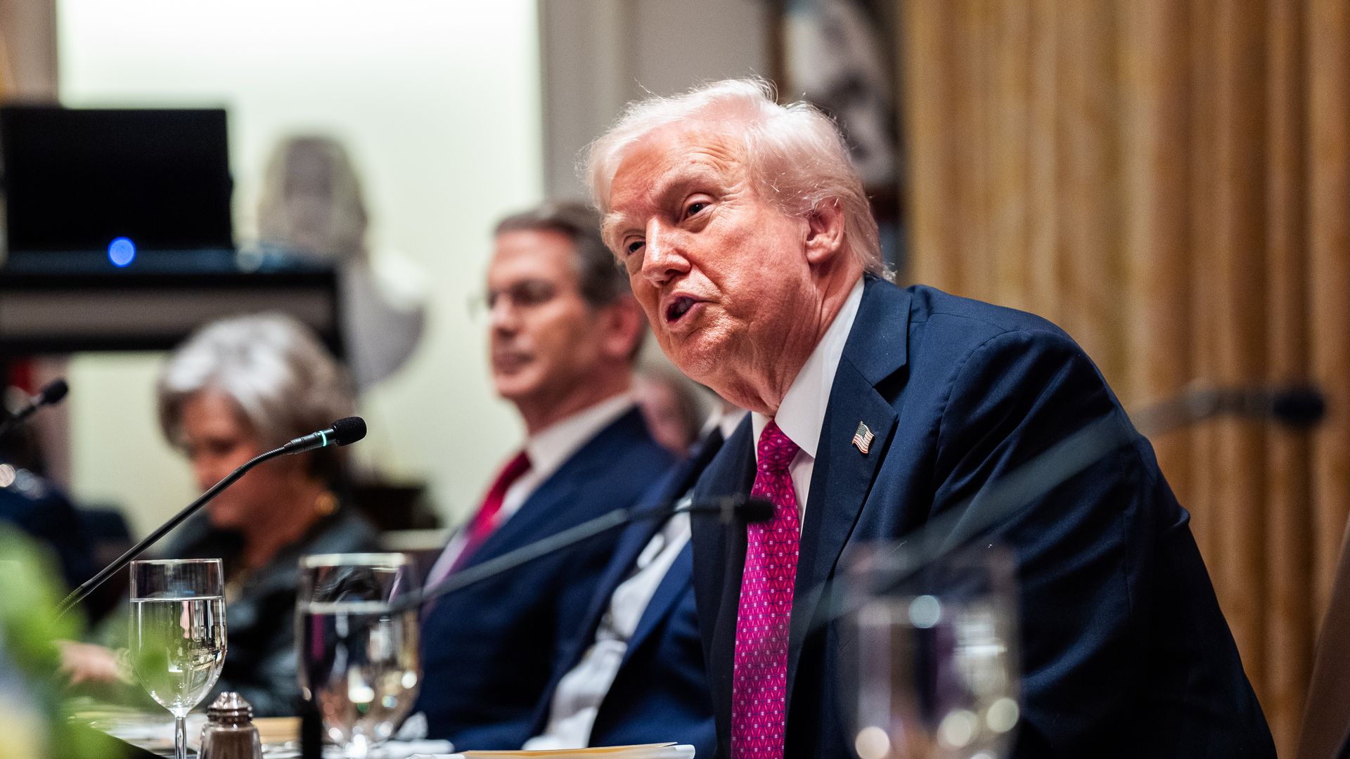 President Trump, seated at a table and leaning into a microphone. 