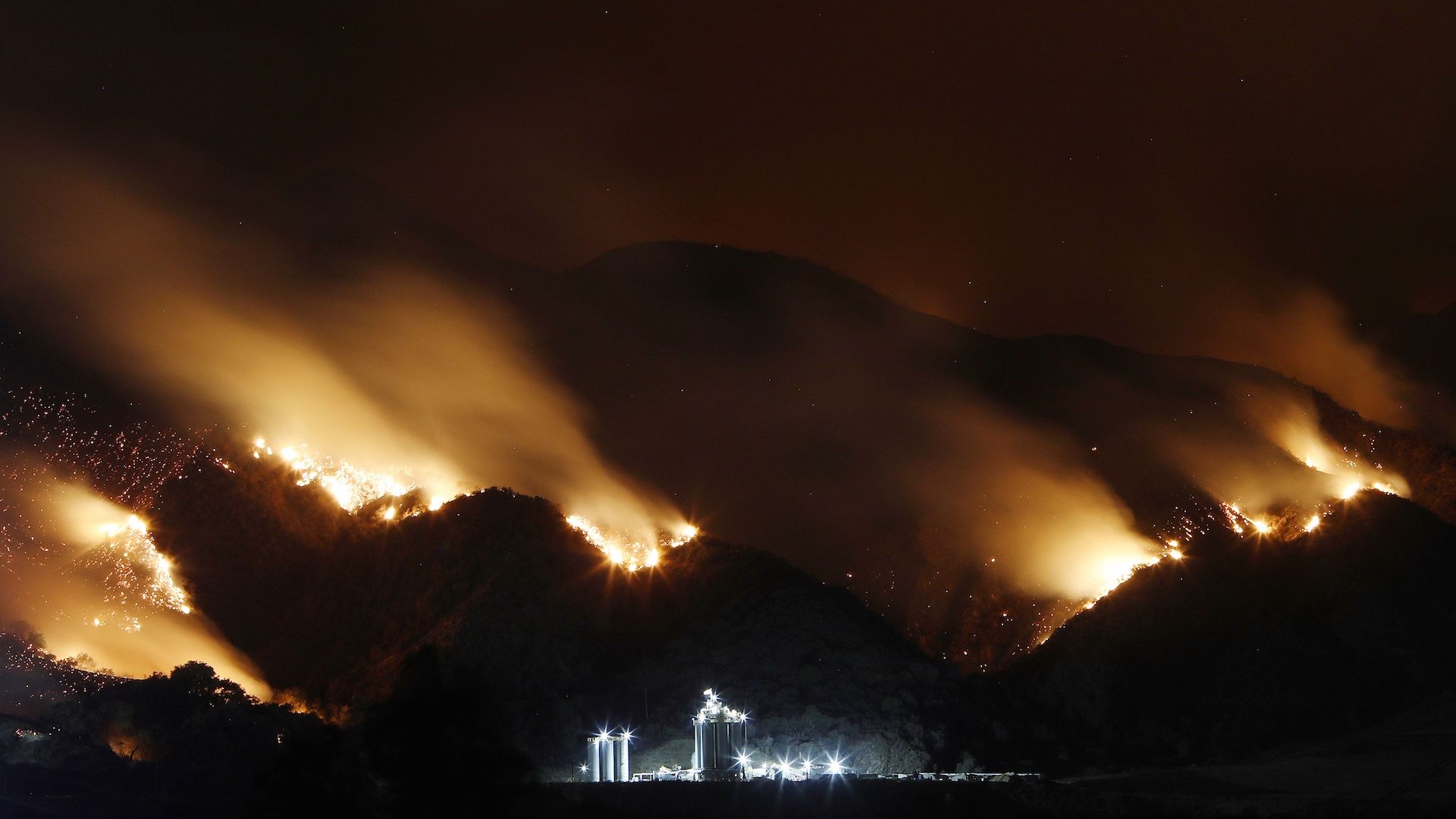 Smoke from the Holy Fire burning in the Cleveland National Forest is blurred in a long exposure above an industrial storage facility on Aug. 10, 2018.