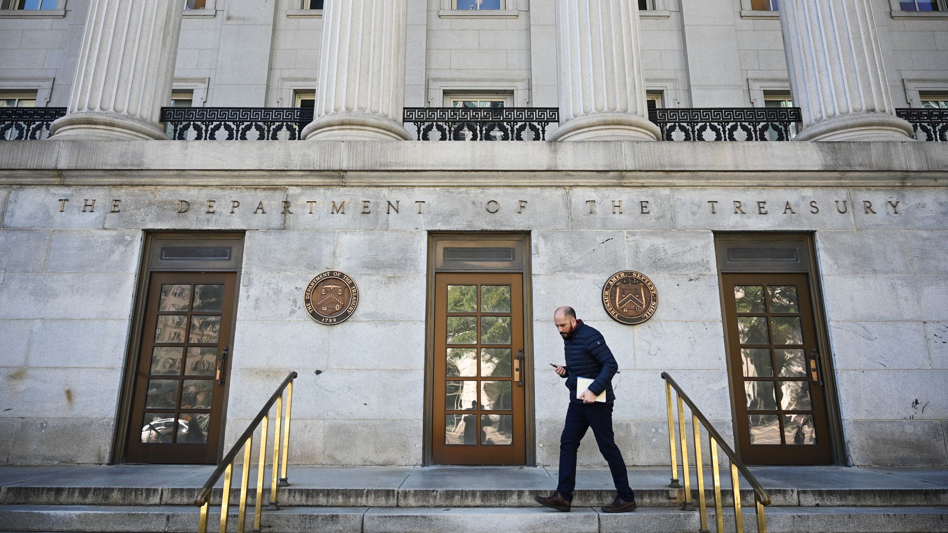 In this image, a man carrying a file walks down the front steps of the Department of Treasury building.