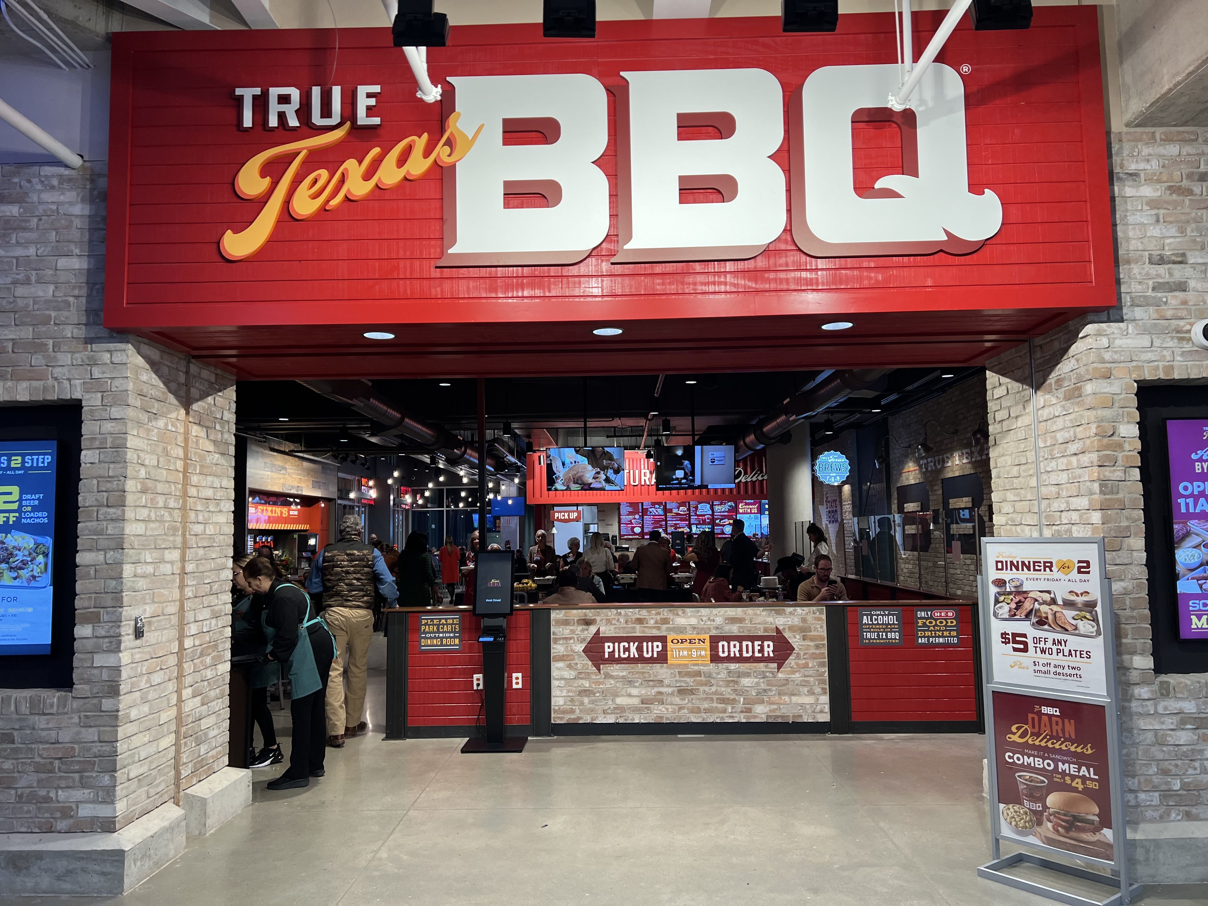A sign that reads "True Texas BBQ" with people in the restaurant under it.
