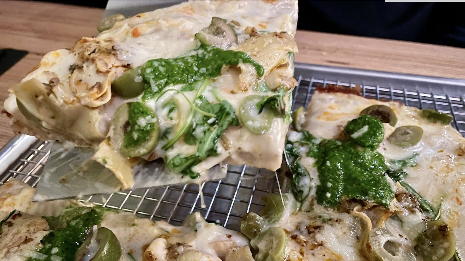A pizza slice with marinated artichokes, olives, pesto and mozzarella cheese. 