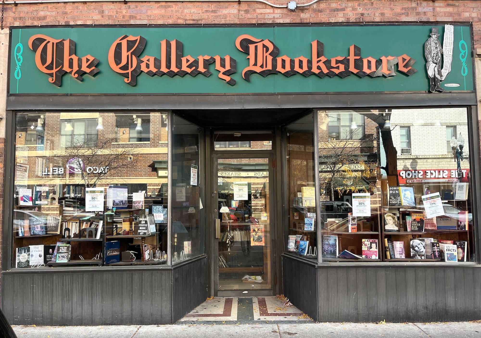 Front of a bookstore with green sign and orange lettering reading The Gallery Bookstore.