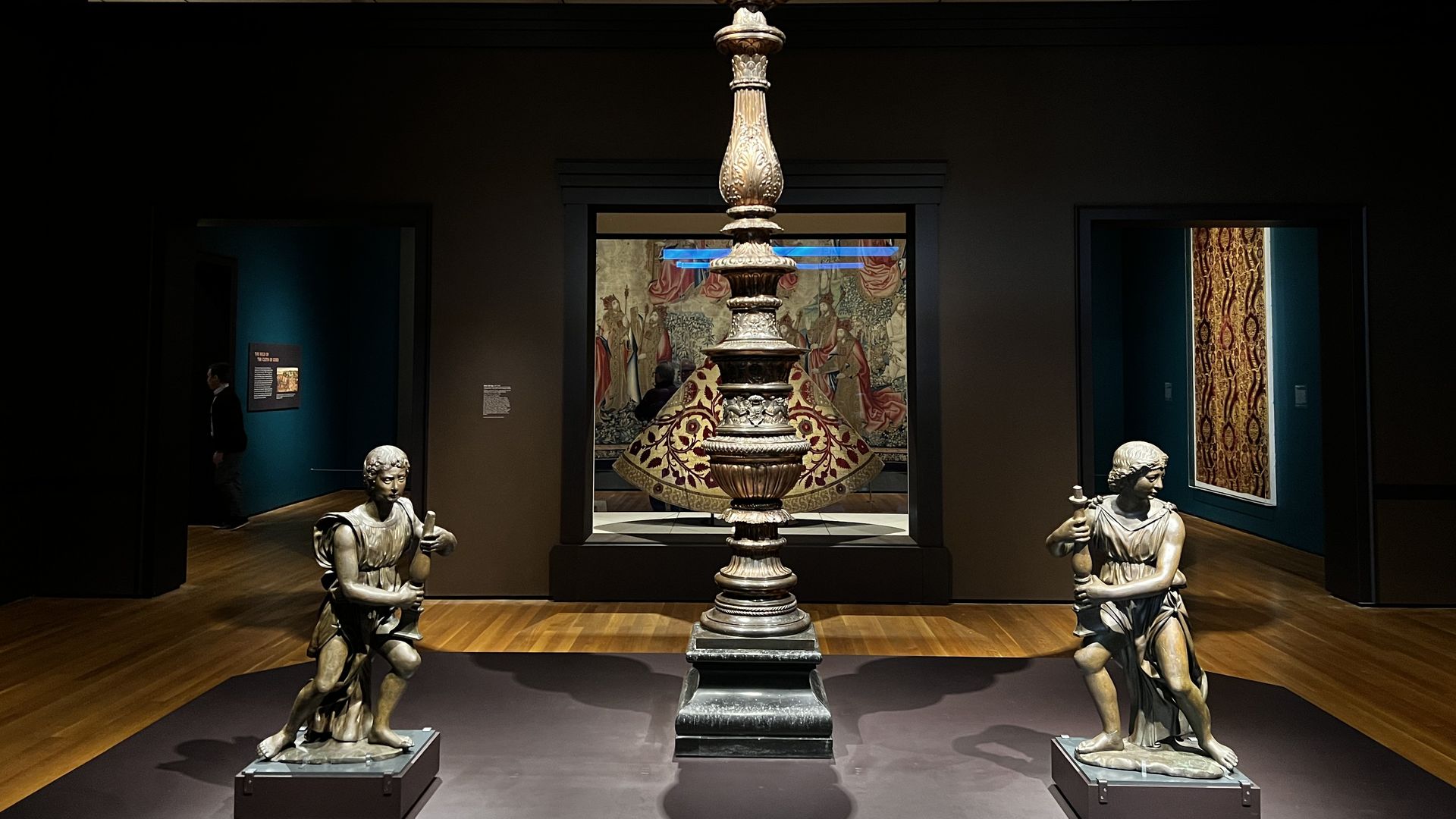 Three statues from the English Renaissance sit in front of a cope in an art exhibit.
