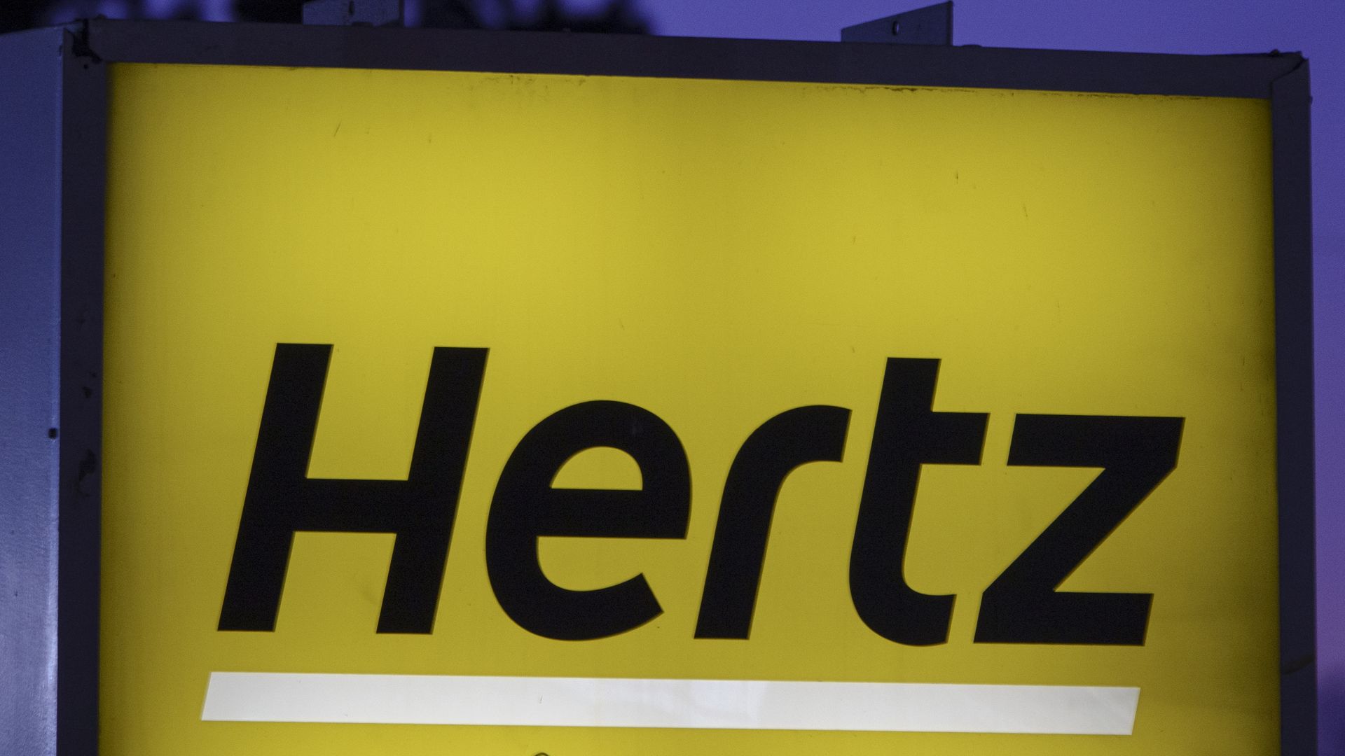 Black letters spelling out Hertz against a yellow backdrop on a lighted sign