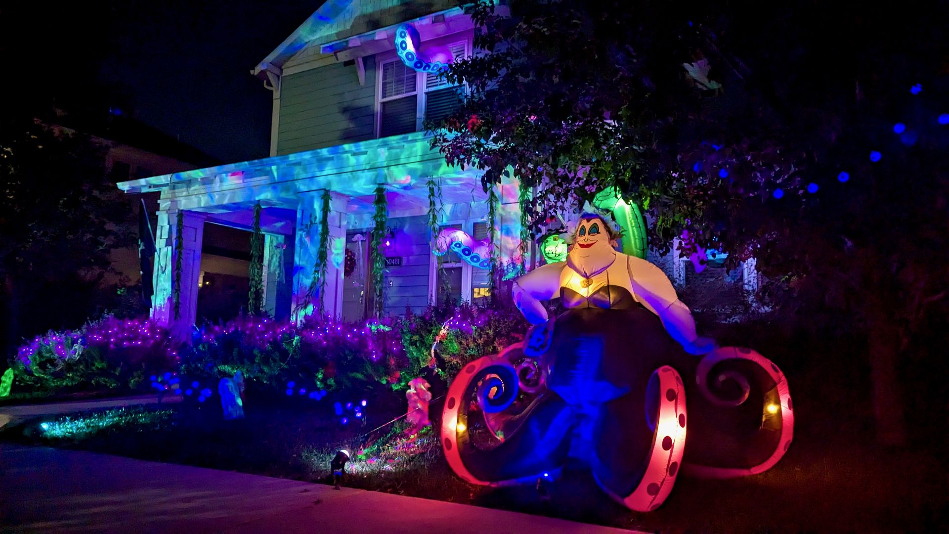 An inflatable decoration of Ursula from Disney's "The Little Mermaid" in front of a house with light projections like water.