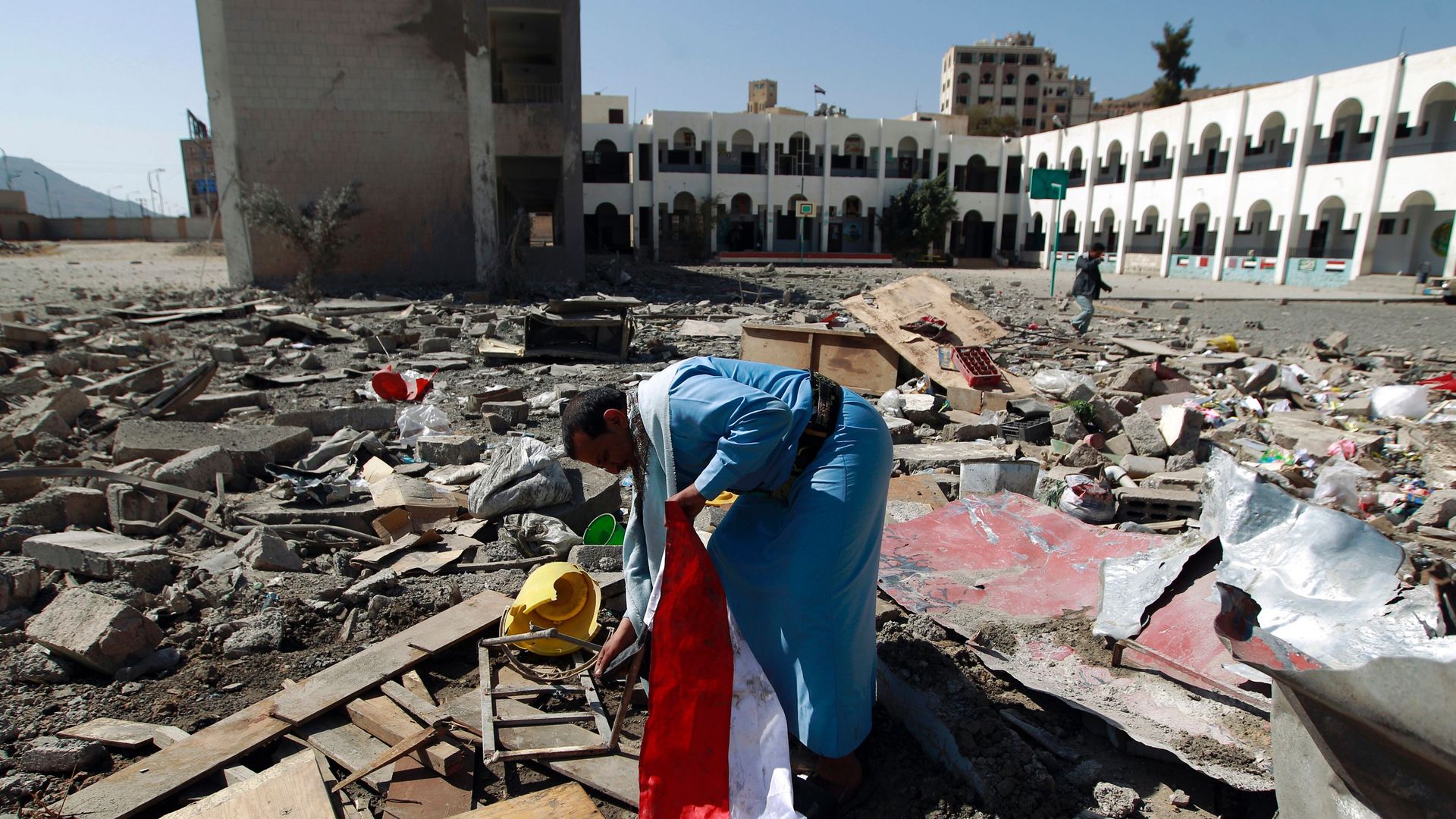 In this image, a man in Yemen holds a flag while searching through rubble. 