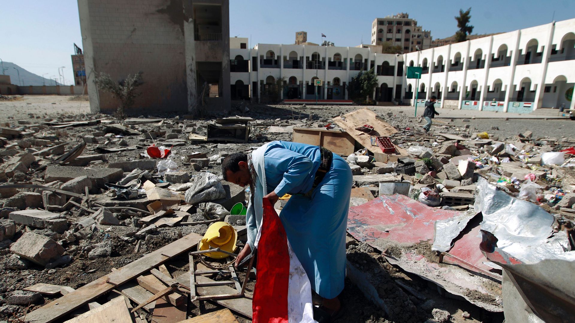 In this image, a man in Yemen holds a flag while searching through rubble.