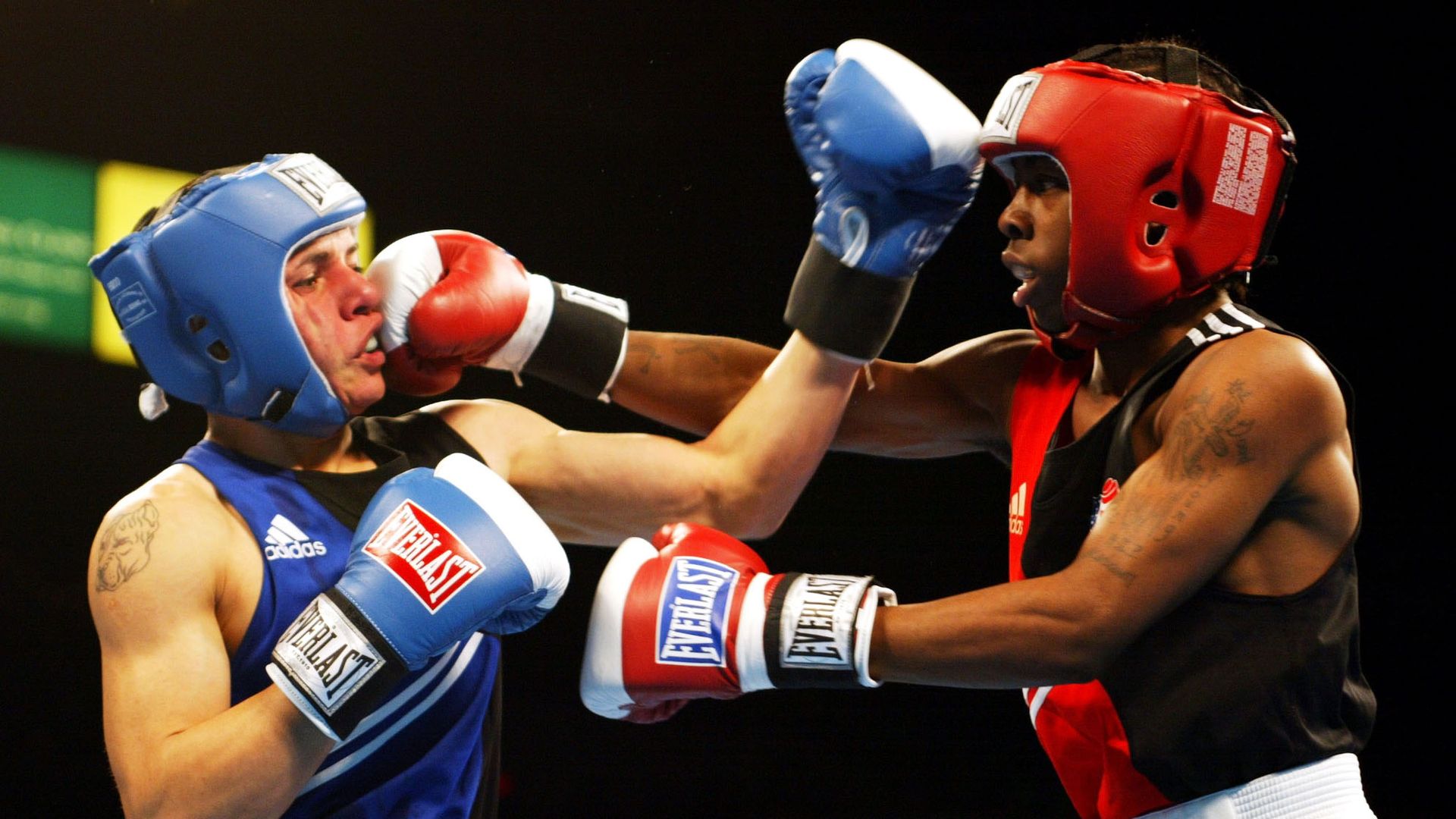 A boxer in blue gloves and head covers fights one in red.
