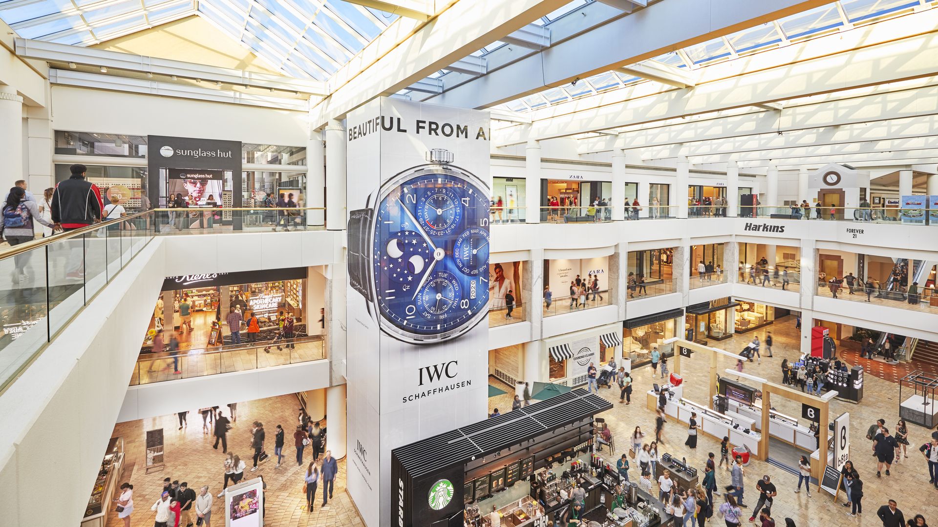 The interior of a three-story, indoor shopping mall, with customers walking around.