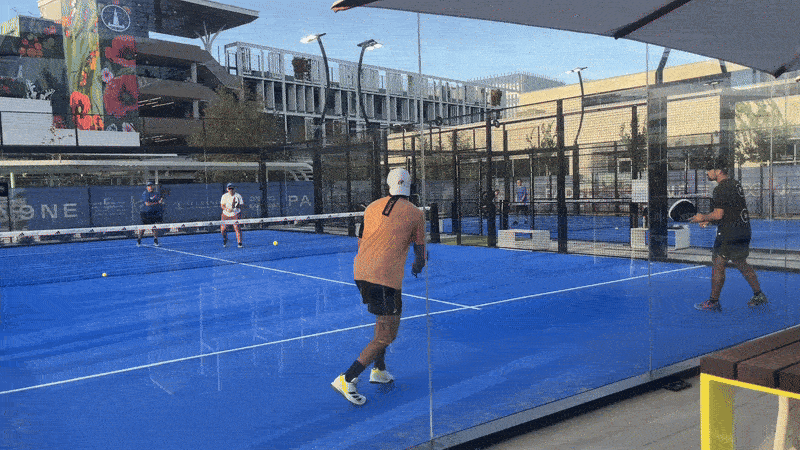 A GIF of four players hitting balls back and forth on a Padel court with blue turf.