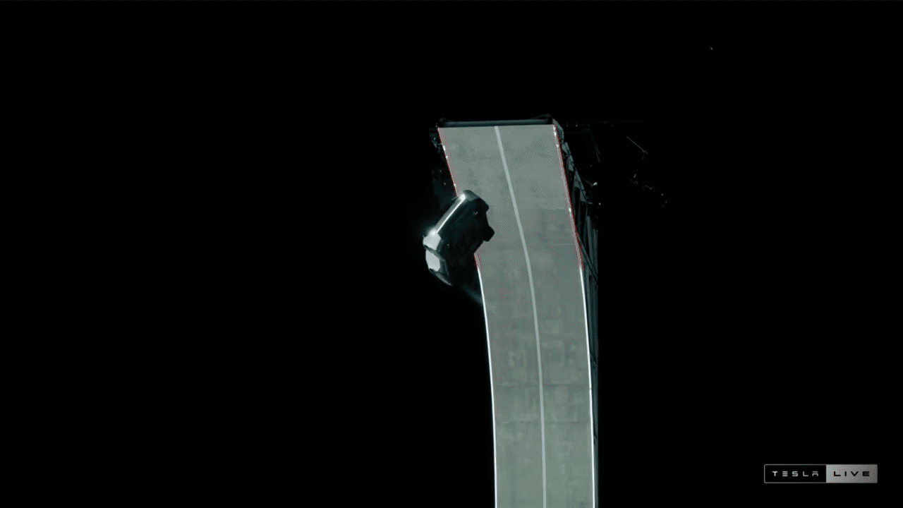 Black background with a tall, curved gray-green ramp; a small silver vehicle sits along the outer curve. Tesla Live watermark appears in the bottom-right.