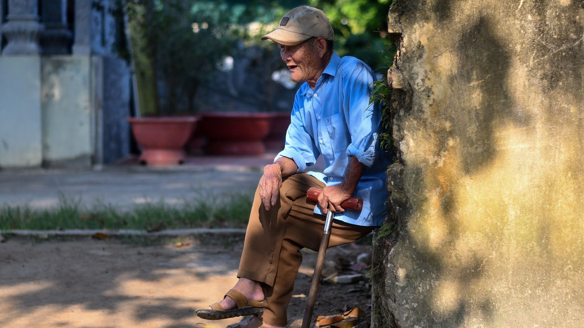 In this image, an elderly man sits outside with a stick in Vietnam