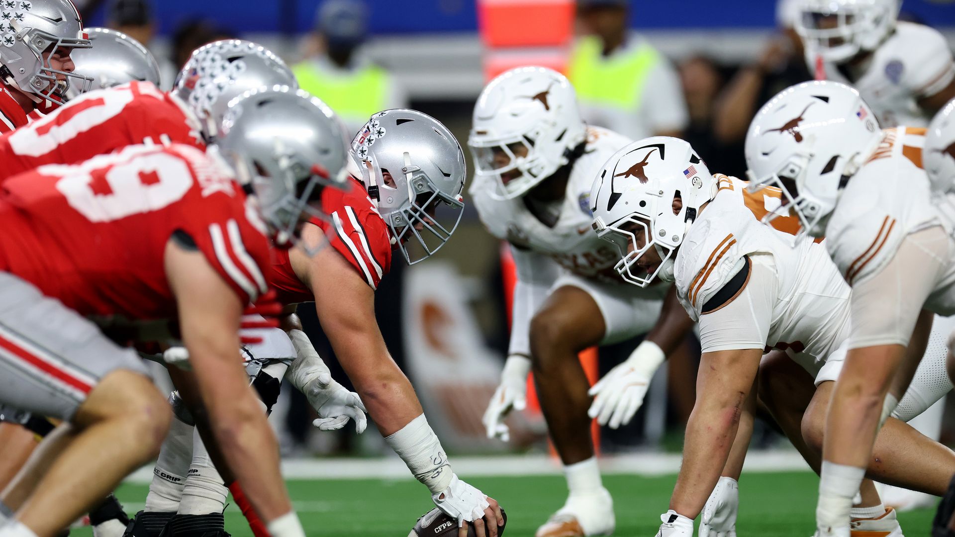 College football players line up on the line of scrimmage; team in red and silver helmets faces team in white helmets with orange longhorn logos.