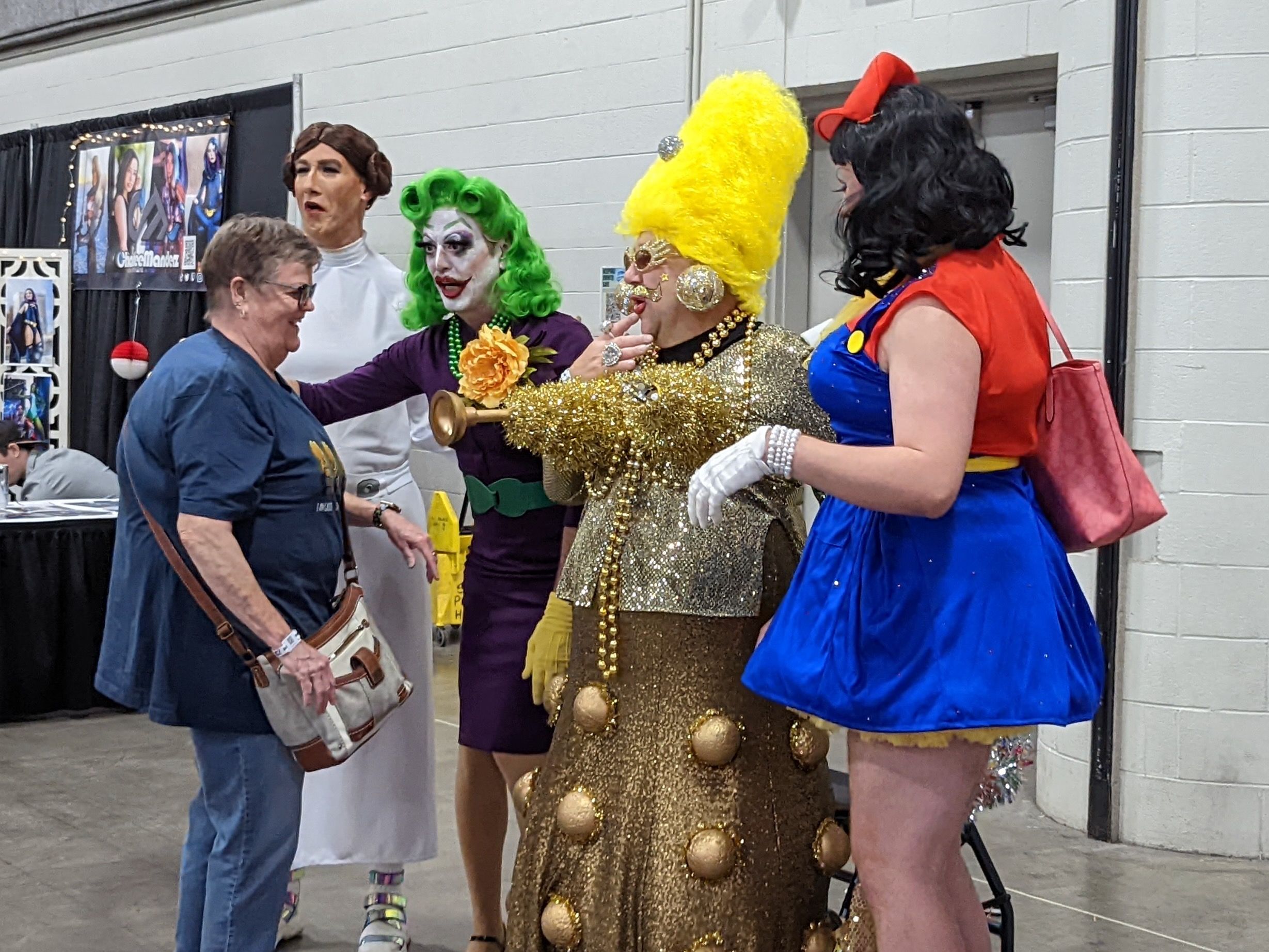 A group of men dressed in drag as Princess Leia and other queens greet a woman with hugs.