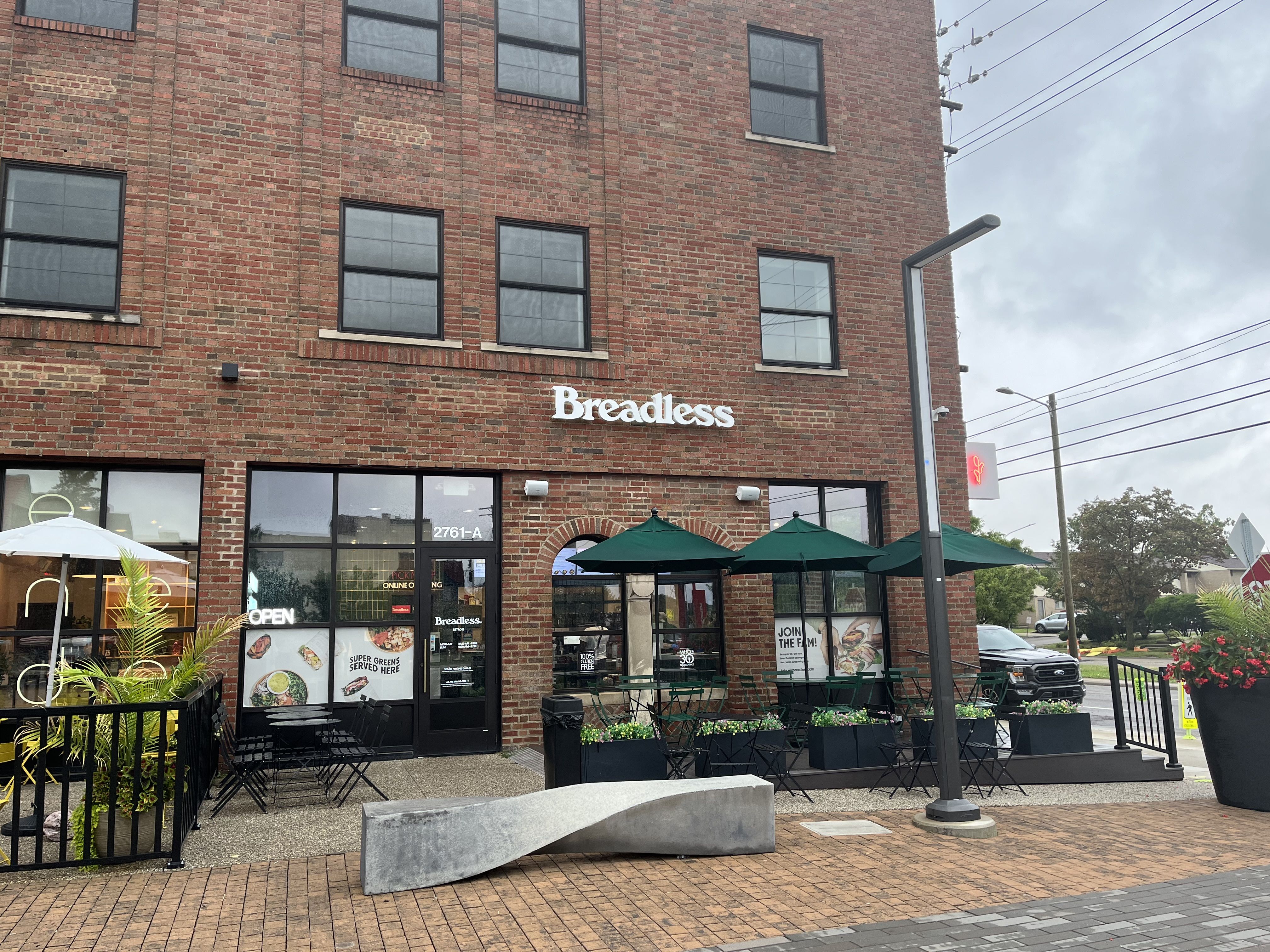 The brick frontage of Breadless, with umbrellas over outdoor seating in front.