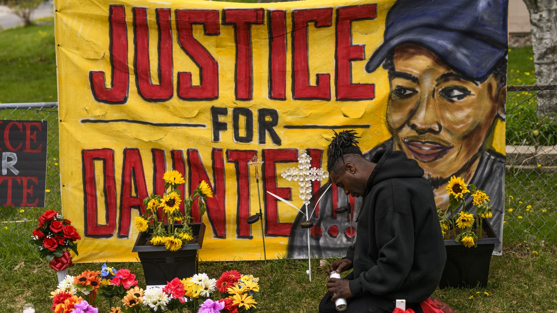 A man lights candles at a memorial for Daunte Wright that has a yellow justice for daunte banner and flowers