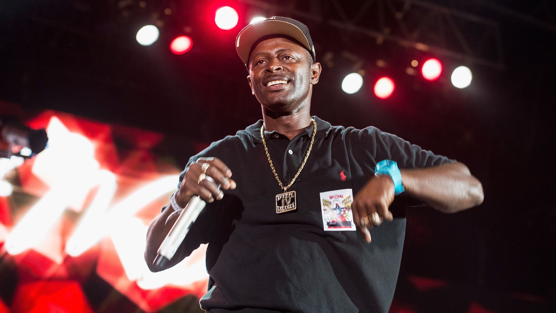 DJ Jubilee performs onstage. He looks out at the crowd, not pictured, and holds a microphone in one hand.