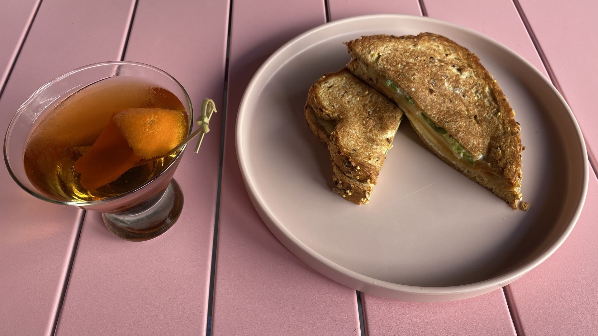A sandwich on a plate next to a brown colored cocktail. 