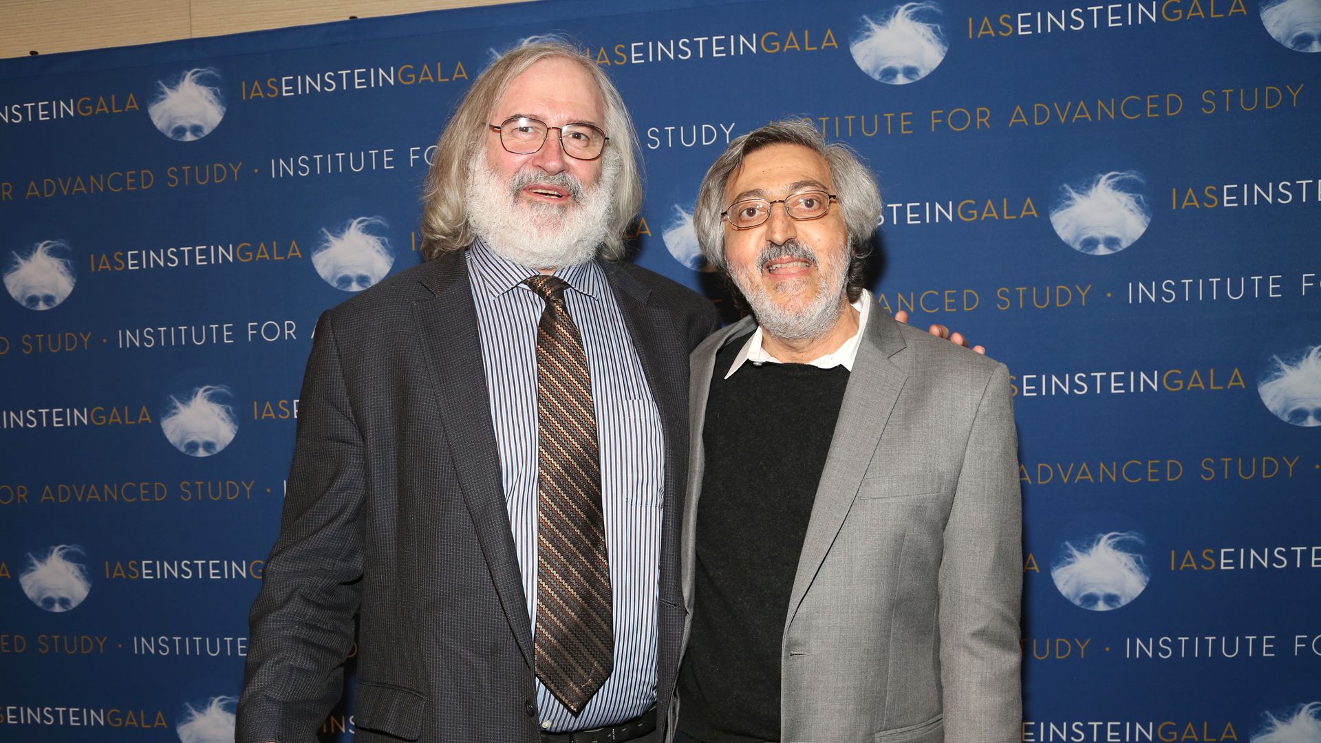 Two men pose for a picture in front of a conference wall.