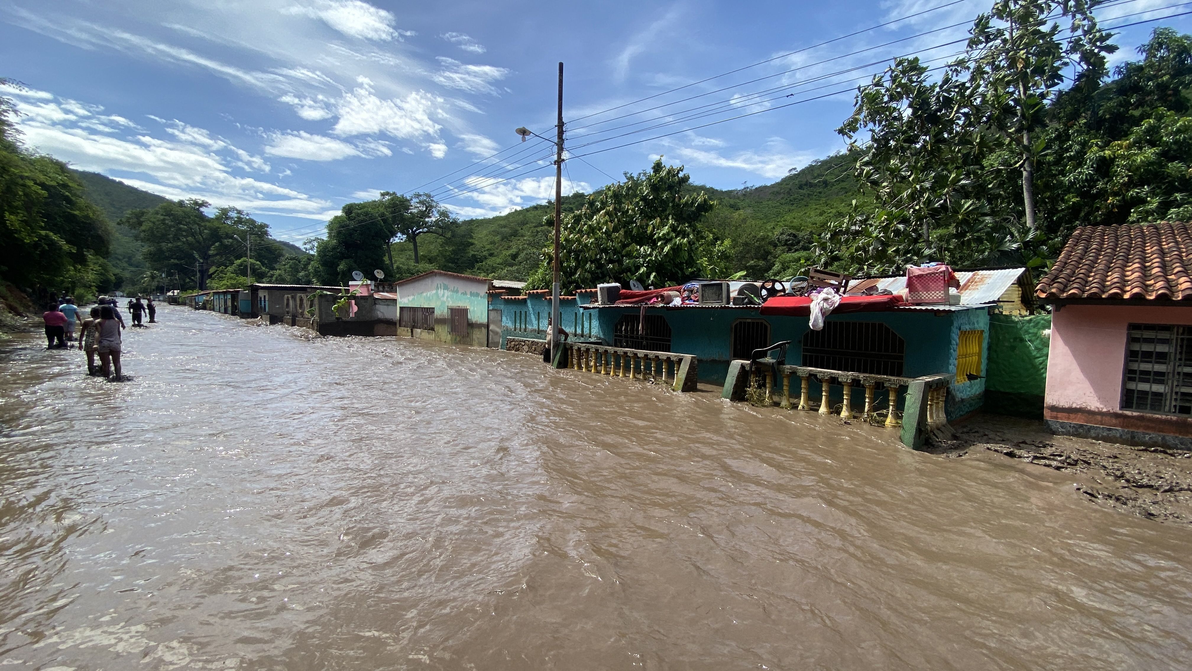 People stand outside their flooded homes after a river swelled due to heavy rains following the passage of Hurricane Beryl on the road from Cumana to Cumanacoa, Sucre State, Venezuela, on July 2, 2024. 