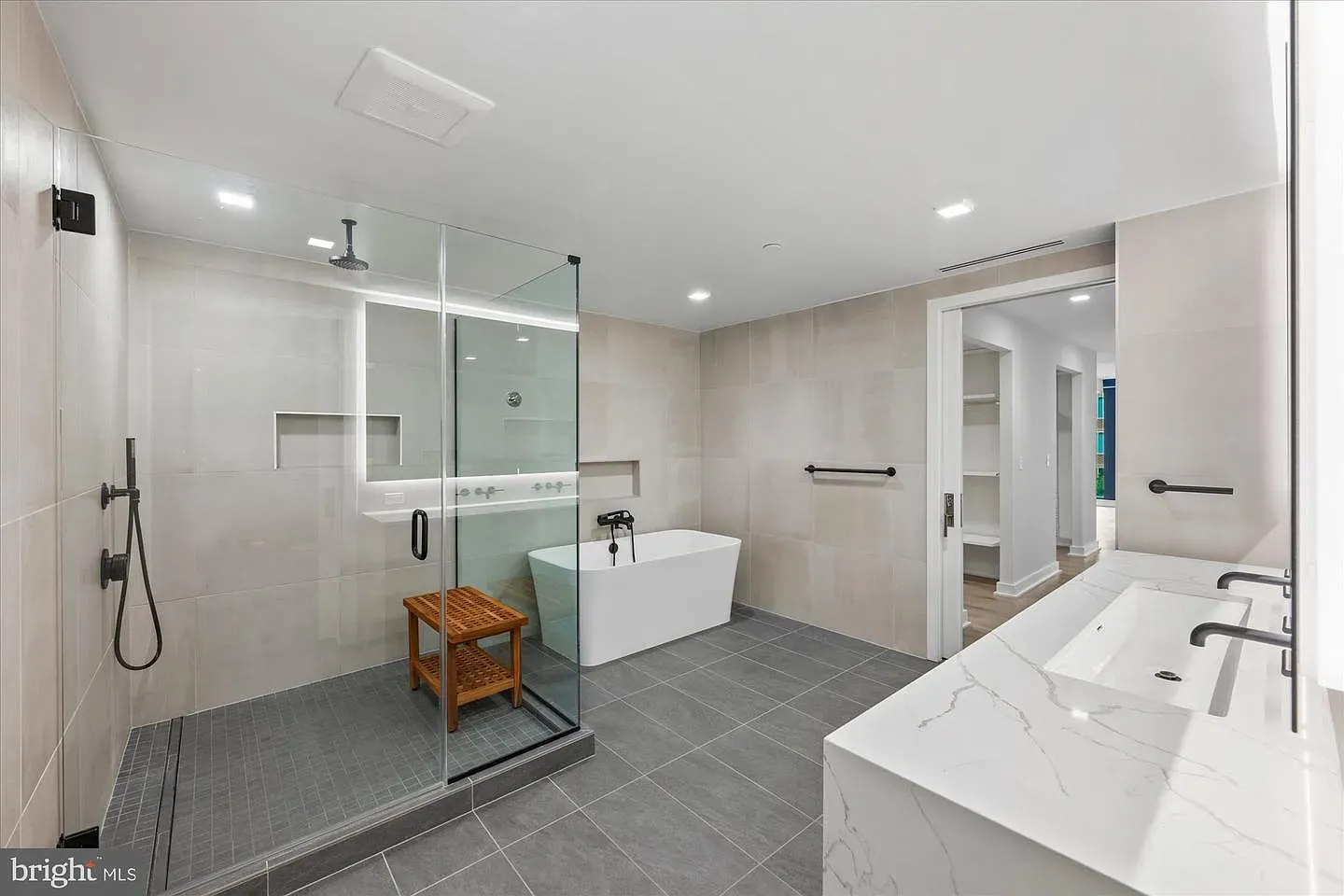 Modern bathroom with a glass-enclosed shower featuring a rainfall head, a white freestanding tub, a marble double vanity, gray floor tiles, beige walls, and black fixtures.