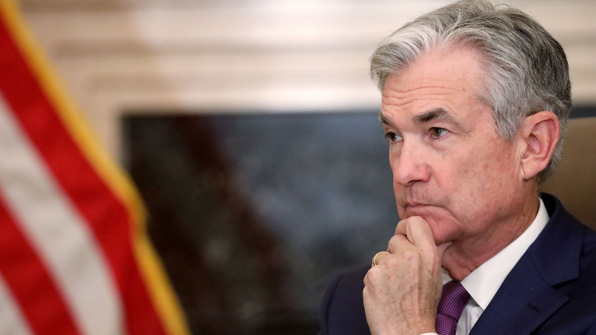 In this image, Powell sits and listens while holding his chin. 